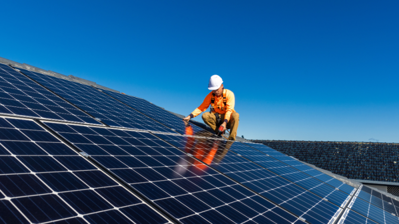 Solar panel technician with drill installing solar panels, sunny day